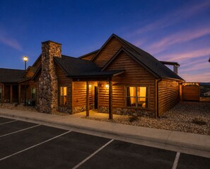 Une cabane en rondins avec une cheminée en pierre, une véranda et un parking.