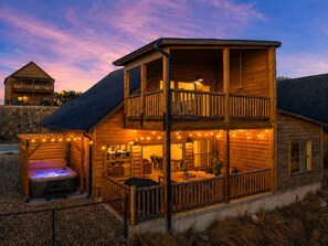 A two-story wooden cabin with a hot tub, outdoor seating, and string lights. - Hot Tub, Pool, Lake Views, King Beds - Sleeps 18 (Branson)