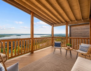 A wooden deck with a view of a lake and distant hills, furnished with wicker chairs and a small table. - Hot Tub, Pool, Lake Views, King Beds - Sleeps 18 (Branson)