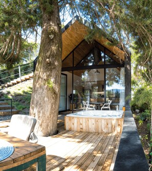 A modern outdoor hot tub area with wooden decking, a glass-enclosed structure, and a staircase leading up. - Tree House: Gorgeous cabin with jacuzzi in Guatape (Peñol)
