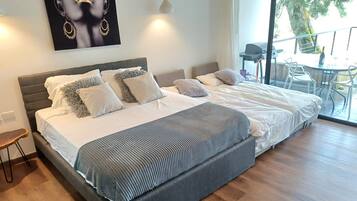A large bed with a grey headboard, multiple pillows, and a striped blanket. There is a small table and chairs outside the window.