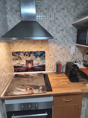 Una cocina con campana de acero inoxidable, salpicadero de azulejos, un cuadro del Arco del Triunfo, cafetera y microondas.