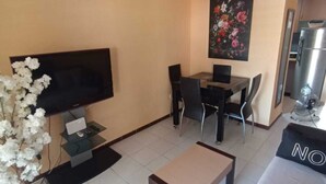 Un espacio habitable compacto con una televisión de pantalla plana, una mesa de comedor con sillas, un sofá y una pequeña mesa de centro.