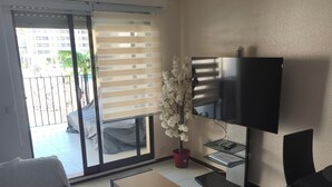 Una sala de estar con un sofá, una mesa de centro, un televisor y un ventanal corredera que da a un balcón.