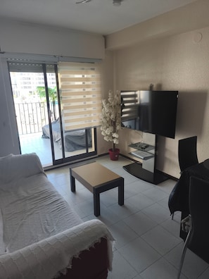 Una sala de estar con un sofá, una mesa de centro, un televisor y un ventanal corredera que da a un balcón.