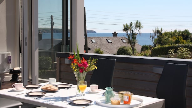 Een ontbijt gedekte eettafel met uitzicht op zee en een balkon.