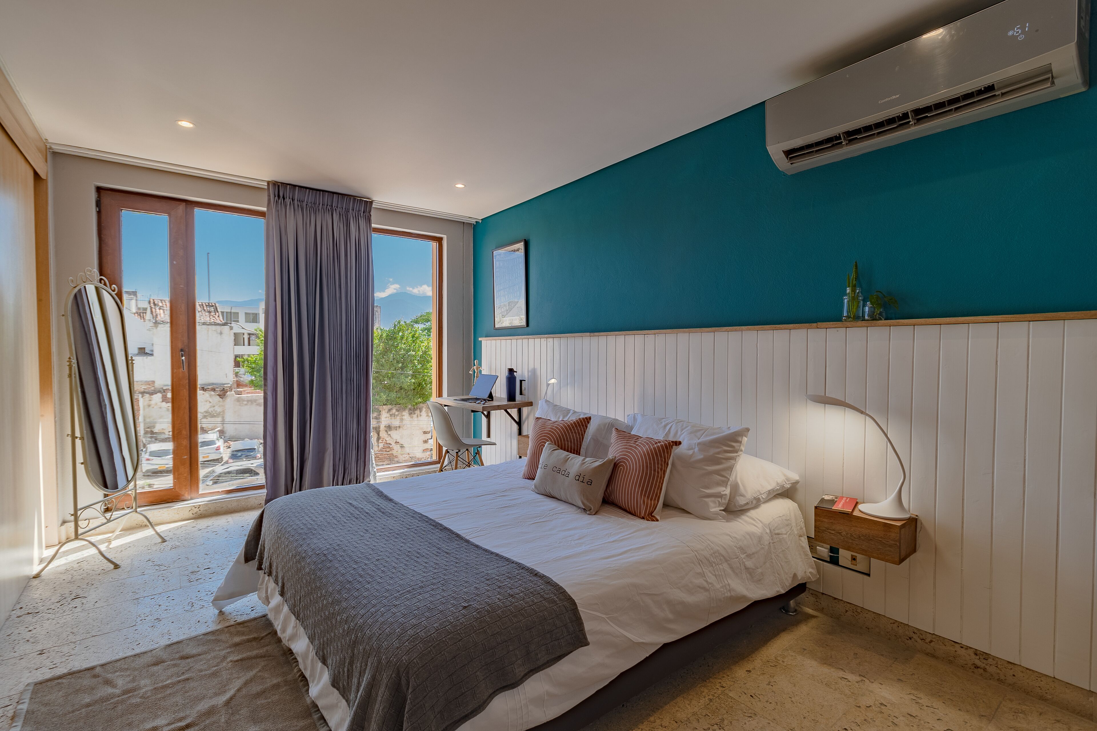A bedroom with a bed, a desk, and a view of the city through a large window.