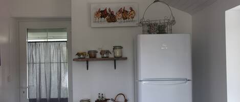 A kitchen with a white refrigerator, a yellow cabinet, and a window with checkered curtains.