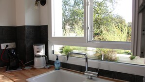 A kitchen with a white sink, a coffee maker, and a window with a view of greenery outside.