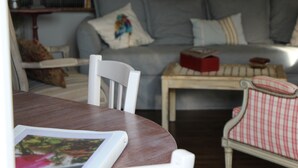 A living room with a wooden table, a white chair, a grey sofa with decorative pillows, and a red and white checkered chair.