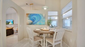 A dining area with a round table set for four, surrounded by white chairs with burlap cushions. A large abstract painting is on the wall above the table. - Heated Saltwater Pool Spa Game Room - Family friendly Tropical Oasis!  (Palm Coast)