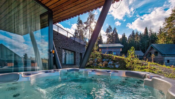 Ein Whirlpool mit klarem Wasser, umgeben von einer Holzterrasse und einem modernen Gebäude mit großen Fenstern.