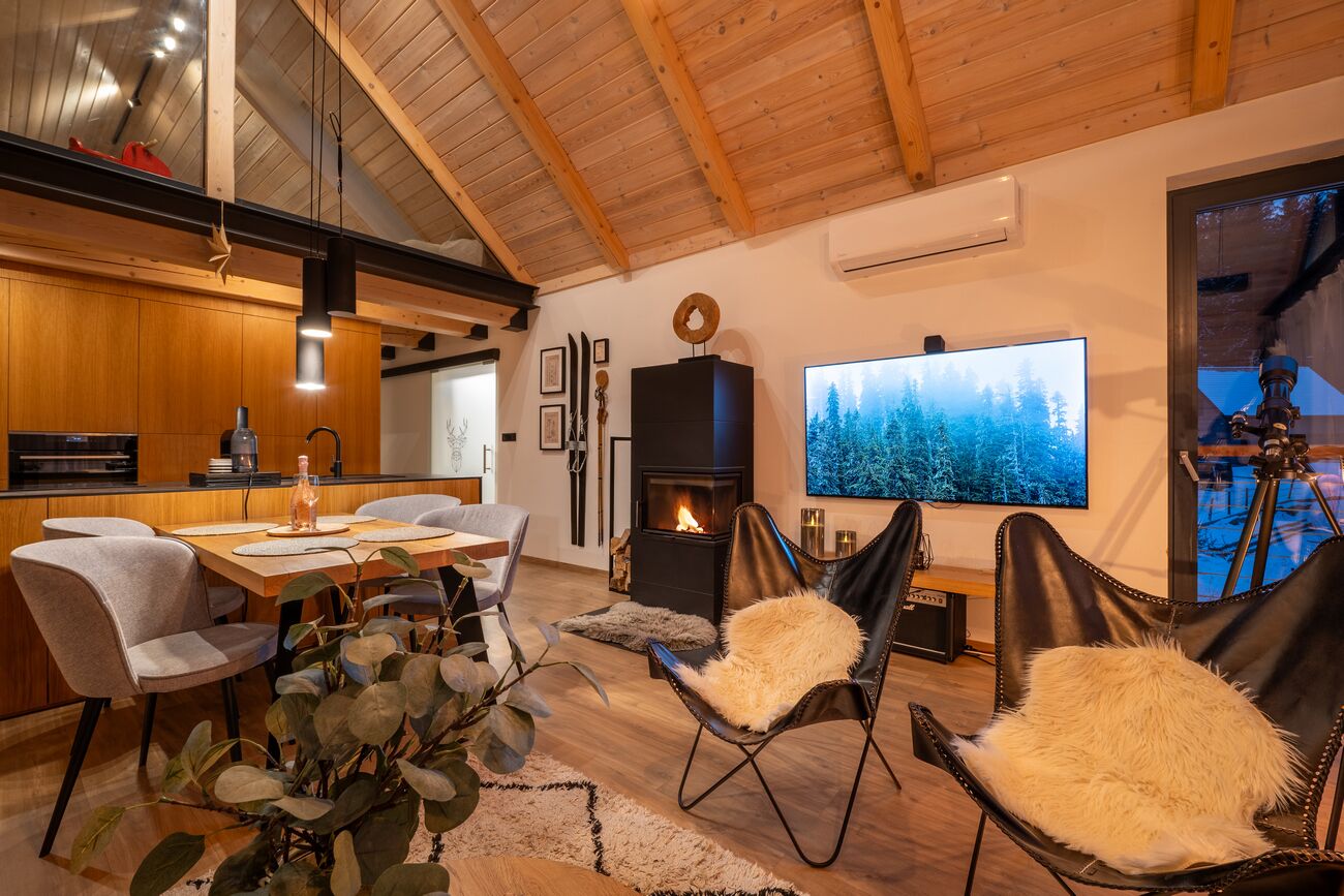 Ein modernes Wohnzimmer mit Kamin, Essbereich und einem großen Fernseher, der eine Waldszene zeigt.
