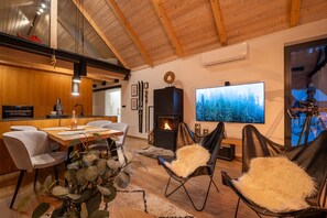 A modern living room with a fireplace, a dining area, and a large TV screen displaying a forest scene.
