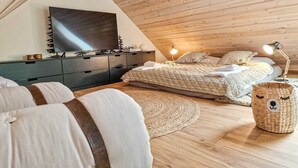 Ein gemütliches Schlafzimmer im Loft-Stil mit einem großen Bett, einem an der Wand befestigten Fernseher und einer Holzbalkendecke.