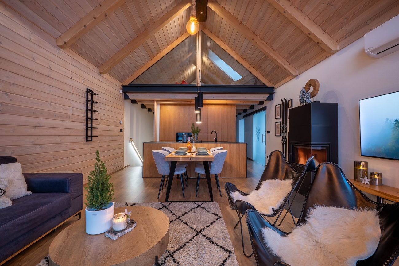 A modern interior with a dining area, leather chairs, a fireplace, and a wooden ceiling.