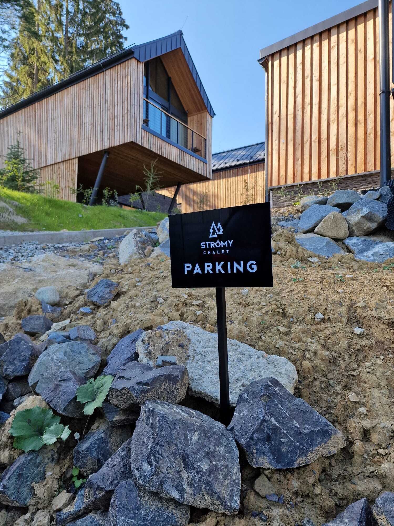 En skylt som visar vägen till parkeringsplatsen för Strömmy Chalet, med en modern byggnad i bakgrunden.