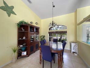 A dining area with a large wooden table, blue chairs, a wooden cabinet with glass doors, and a window with a view of the outdoors. - Turtle Bay, full refund*, pool heat, dogs ok, pool (Rotonda West)