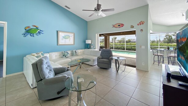 A living room with a light blue wall, a white sofa, a grey armchair, a glass coffee table, and a ceiling fan. - Turtle Bay, heated pool, 2 dogs ok, pool table (Rotonda West)