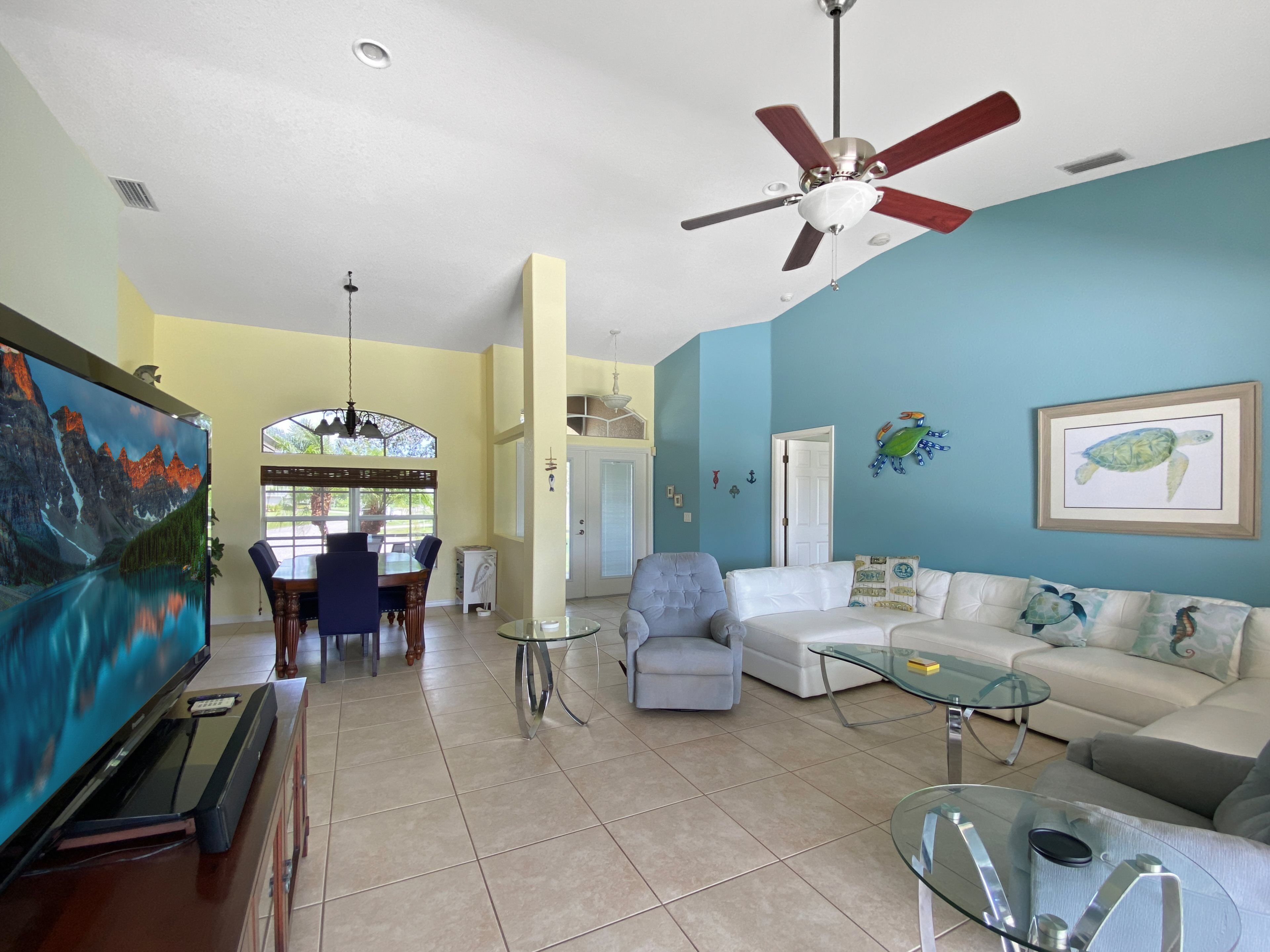 A spacious living room with a ceiling fan, a dining area with a view, and a large painting on the wall.