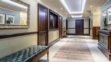 A hotel hallway with a bench, doors, a mirror, and a ceiling with skylights.