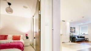 A bedroom with a bed, bedside table, and a nightstand. There is a hallway leading to a living area with a sofa and a coffee table. - Cathedral Quarter | City Centre | Walk Everywhere - Pass the Keys (Belfast)
