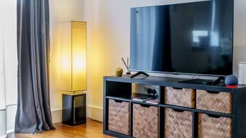 A modern living room with a large flat-screen TV, a floor lamp, and a herringbone-patterned storage unit.