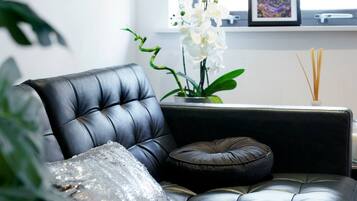 A black leather sofa with a sequined pillow and a dark cushion, a small potted orchid, and a picture frame on a shelf.