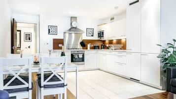 A modern kitchen with white cabinetry, a stainless steel range hood, and a built-in oven.
