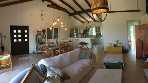 A spacious living area with a large white sofa, a dining table, and hanging light fixtures. - A beautiful olive orchard with mountain and sea view,ideal for a relaxing break  (Ziria)
