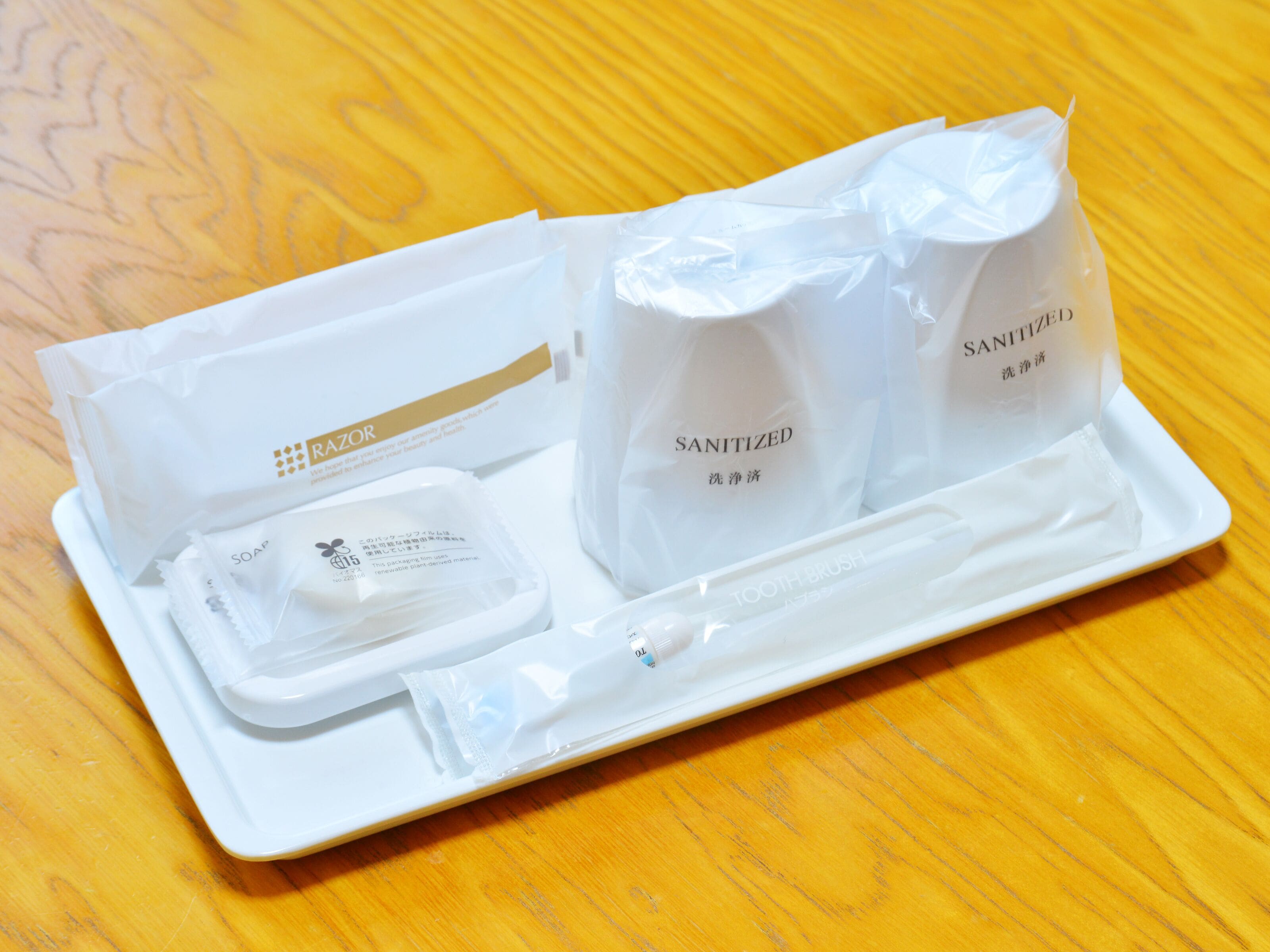 A tray with a razor, soap, and two bags of sanitizer on a wooden surface.