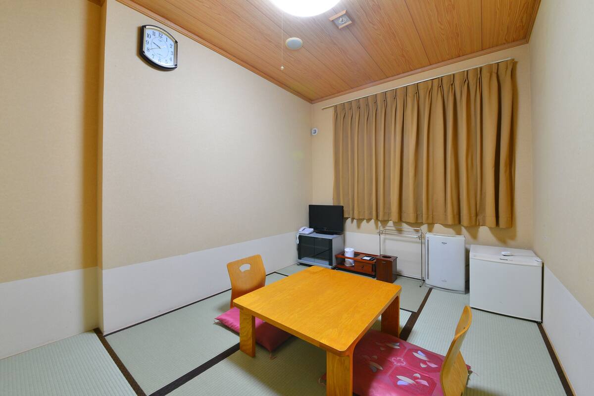 A small room with a wooden table, chairs, a television, a small cabinet, and a clock on the wall.