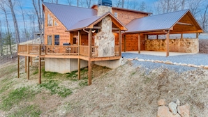 Une cabane en rondins avec une cheminée en pierre, une terrasse en bois et un espace extérieur couvert.