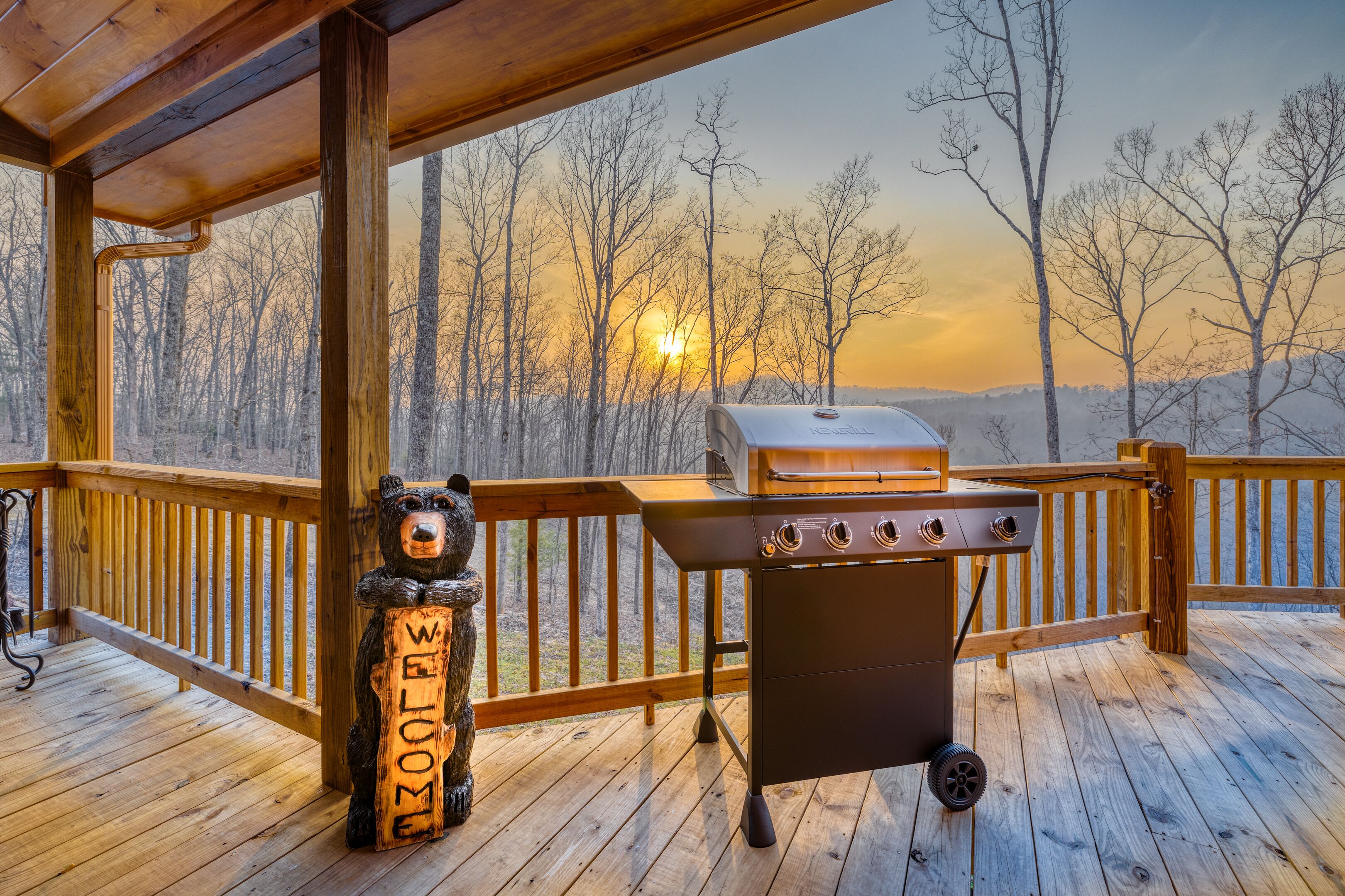 A wooden deck with a grill and a bear-shaped welcome sign.
