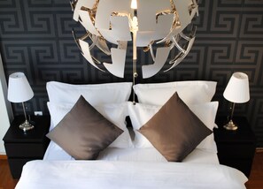 Een net opgemaakt bed met witte lakens en twee bruine kussens, aan weerszijden voorzien van nachtkastjes met lampen, tegen een muur met een geometrisch patroon.