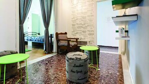 Habitación de hotel con cama, una silla, una mesita y una pared original con nombres de ciudades.