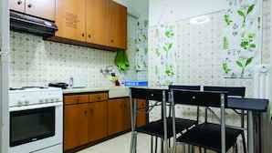 Una cocina con armarios de madera, una estufa y una zona de comedor con sillas metálicas.