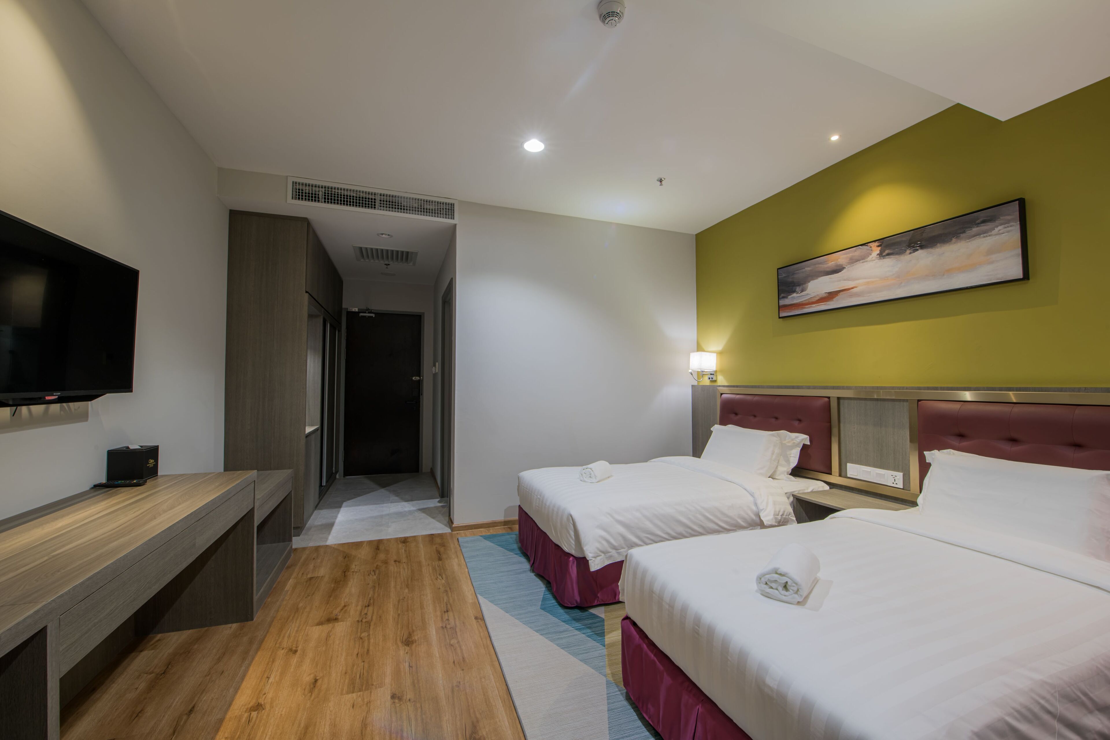 A hotel room with two beds, a TV, a desk, and a painting on the wall.