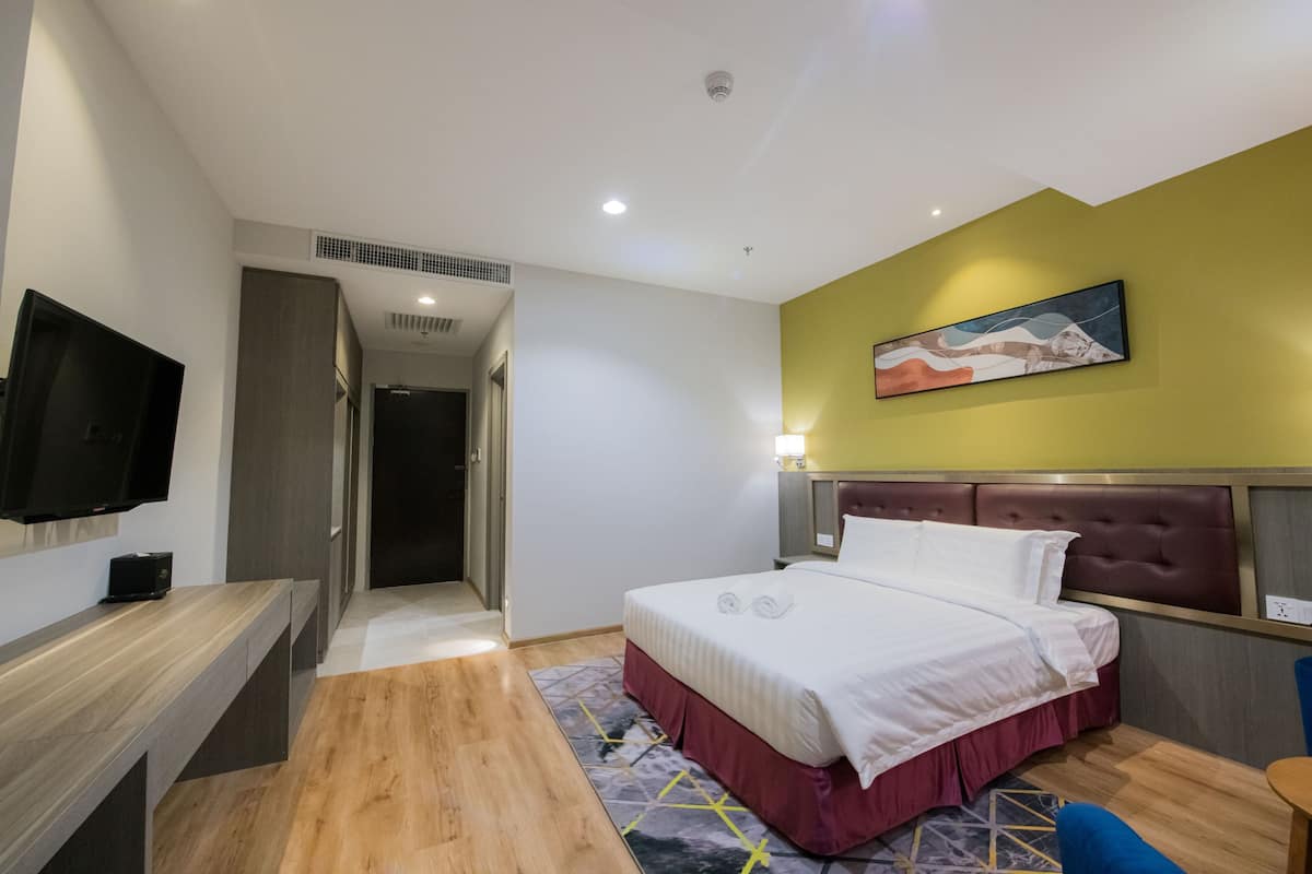 A hotel room with a bed, a desk, a TV, and a painting on the wall.
