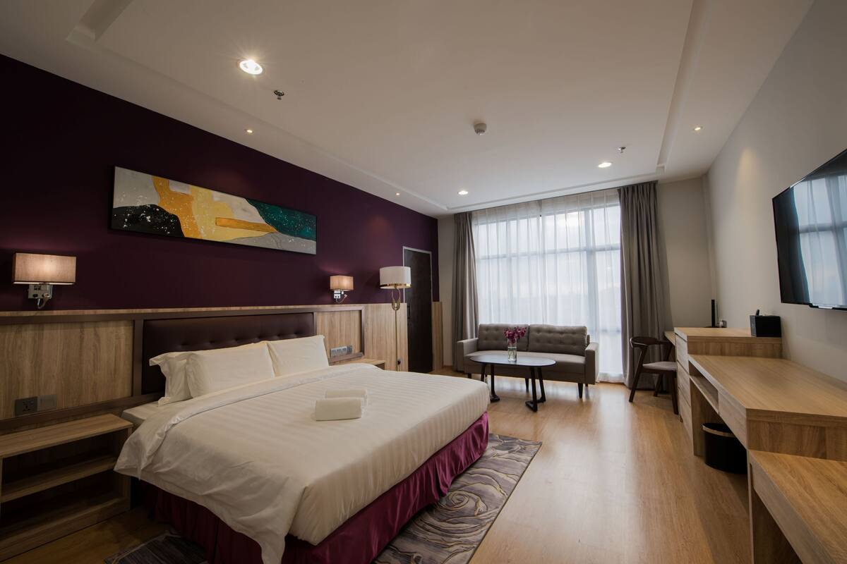 A hotel room with a large bed, a desk, a sofa, and a TV.