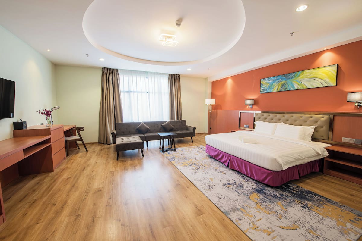 A modern hotel room with a large bed, a desk, a sofa, and a view of the city.