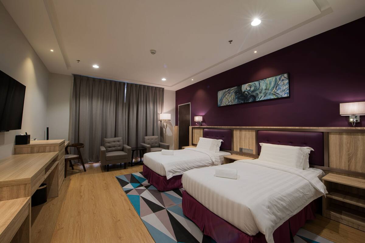 A hotel room with two beds, a desk, a chair, a TV, and a painting on the wall.