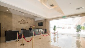 Zona de recepció d'hotel amb sòl de marbre, taulell de recepció i una barrera de corda vermella.