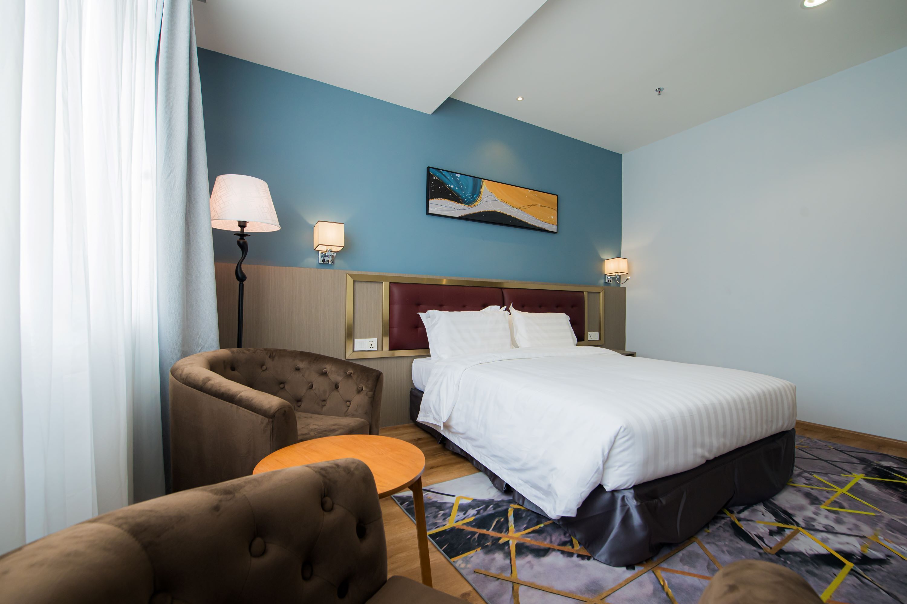 A hotel room with a bed, two armchairs, a small table, and a painting on the wall.
