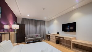 Habitació d'hotel amb un llit gran, una taula de treball, un sofà, una televisió i un bany.