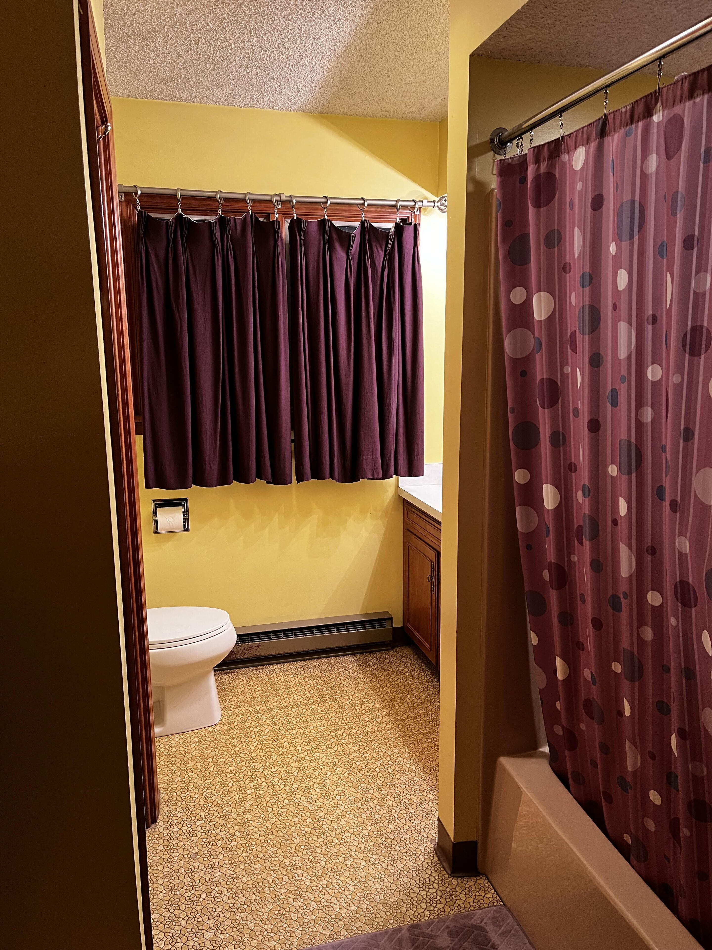 A bathroom with a toilet, a shower curtain with a polka dot pattern, and a tiled floor.