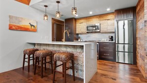 Una cocina moderna con armarios de madera, electrodomésticos de acero inoxidable y una isla central con taburetes de bar.