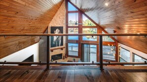 Interior de madera con techo inclinado, ventanas grandes y vistas a una terraza y zona exterior.