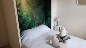 Un dormitorio con una cama, una lámpara, un peluche y un cuadro de un bosque.