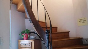 Una escalera de madera con barandilla, un mueble pequeño con cajones y una planta en maceta en el rellano.